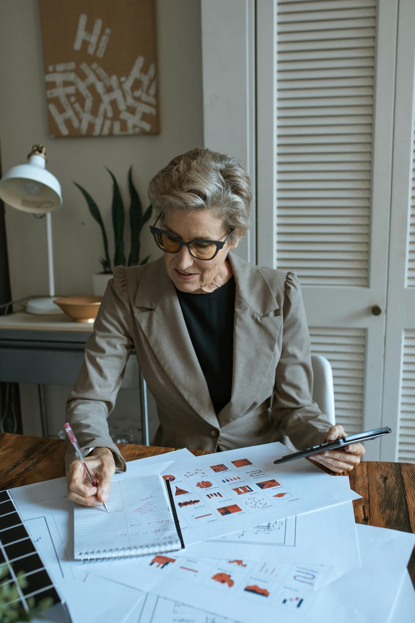 A senior woman analyzing printed data charts in a modern home office setting.